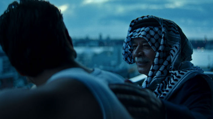 An older man in a keffiyeh speaks with a younger man on a rooftop in If Birds Believed in God (2026).