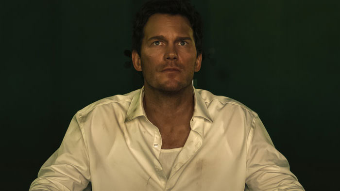 Man in a white dress shirt sits under harsh green lighting in a futuristic courtroom setting in Mercy (2026).