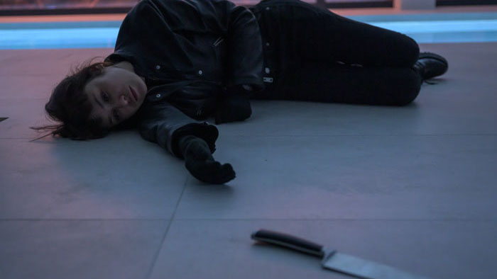 Olga Kurylenko as Sara Black lies on the floor with a knife in the foreground in Misdirection (2026).