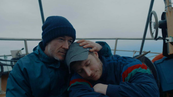 Jack (Barry Ward) holds Daniel (Lorne MacFadyen) aboard a fishing boat in a still from On the Sea (2025) 