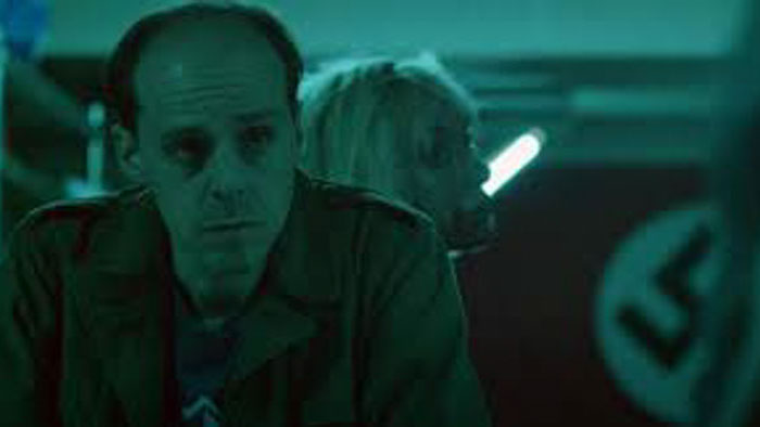 Green-lit close-up of a tense man inside the pawnshop in Red Night at Skye’s (2026). 