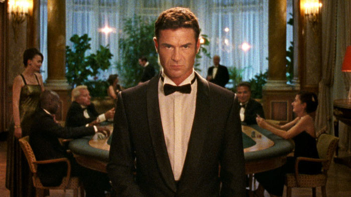 Yannick Renier in Reflection in a Dead Diamond (2025), standing in a tuxedo in a glamorous casino-like room.