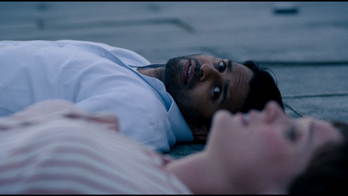 Dev (Asif Ali) and Mary (Bella Heathcote) lie on a rooftop, exhausted, as they struggle to survive in Roof (2025).