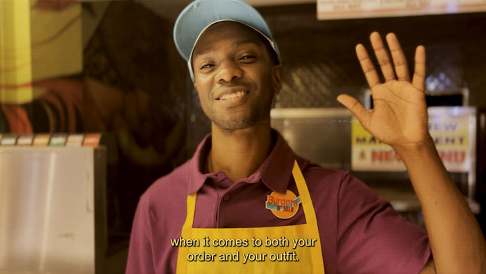Burgers ’n’ Such employee in uniform waves from behind the counter in Secret Menu Beauty Pageant
