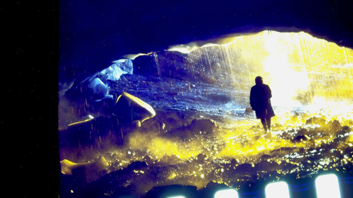 A figure stands inside a glowing glacial ice cave in Time and Water (2026).
