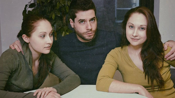 Three characters sit at a table in Videola (2025). 