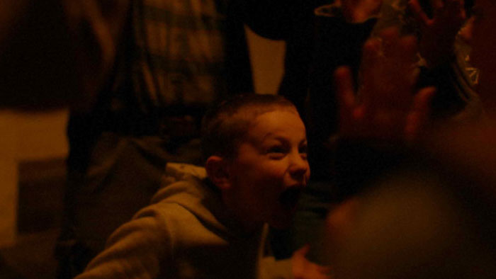 A child in a dim room shouts while adults stand nearby.