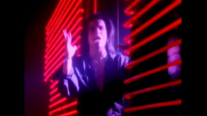 A singer performs in a neon-lit music video clip in Attack Of Life: The Bang Tango Movie.