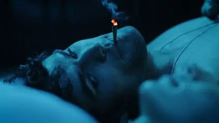 Dark Distortion (2026) still of a person lying in bed under blue lighting with a lit cigarette Title: Dark Distortion (2026) – Blue-lit Bedroom Still