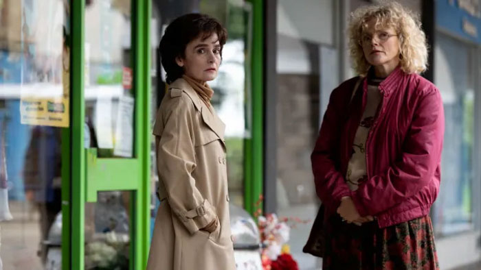 Heather Davidson (Shirley Henderson) stands with Dotty (Maxine Peake) outside a storefront in I Swear (2025).