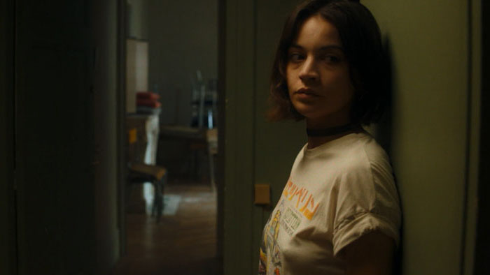 Mahé (Inès Spiridonov) stands in a dim hallway inside an abandoned building in Impure (2026).