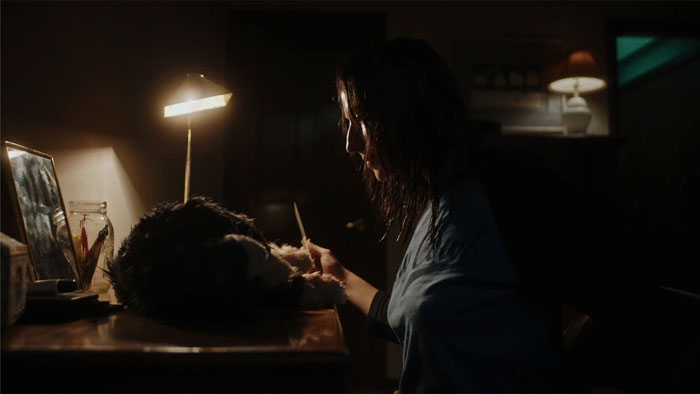 Janet Mancini removing nail polish from Tori’s body in a dimly lit room in Puke Bitch (2026)