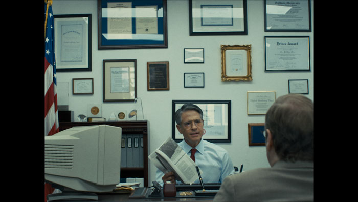 Dr. Fauci sits behind a desk in an office lined with framed certificates in Silence = Death.