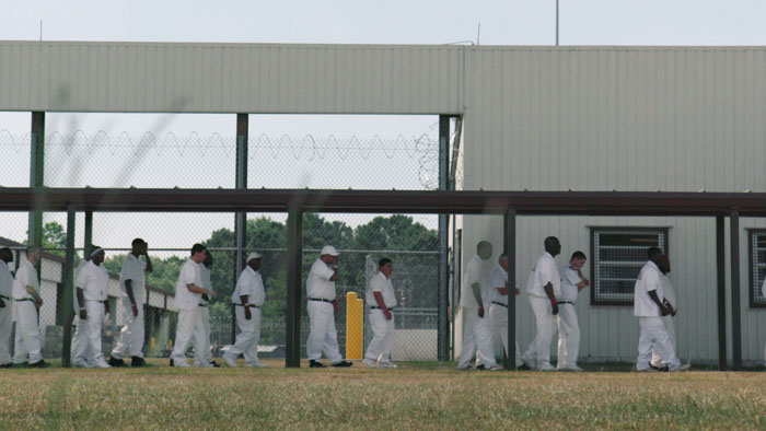 Incarcerated men in white uniforms walk in a prison yard at an Alabama correctional facility