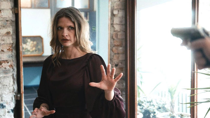 Syama Rayner as Ester confronted at gunpoint in The Art of Telling Lies (2026)