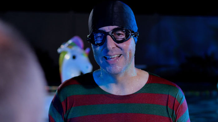 Man in swim cap and goggles wearing a striped shirt in a backyard pool at night 