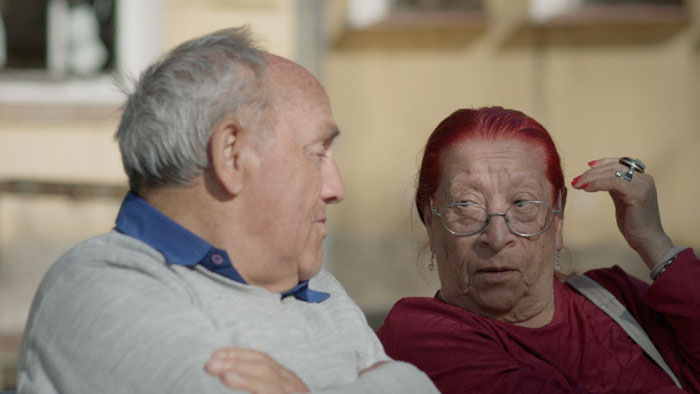 Two elderly residents sit together on a bench in Cuidadoras. 
