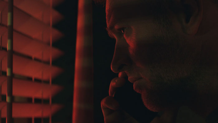 Luca (Matthew Ninaber) peers through window blinds in Death Cycle.