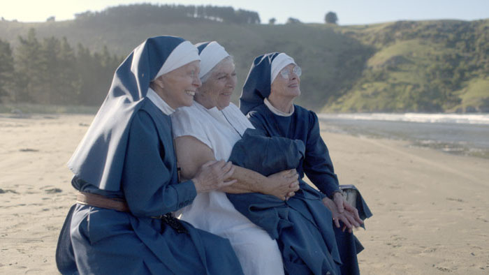 Sister Agnes (Judy Davis), Sister Mary Clare (Jacki Weaver), and Sister Luke (Miriam Margolyes) sitting arm in arm on a New Zealand beach in Holy Days.