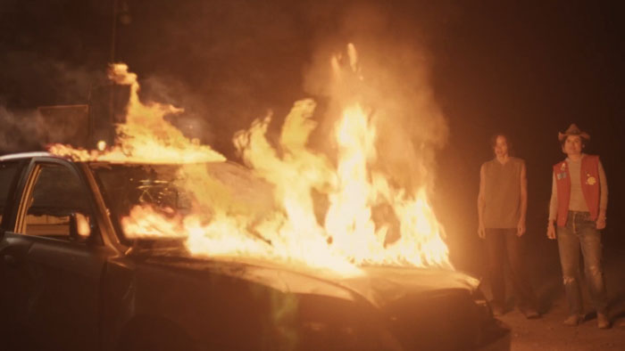 Kai (Ashley Moore) and Sunny (Lío Mehiel) stand near a burning car in Perfect.