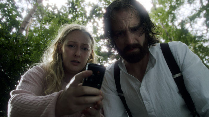 Marie (Mackenzie Larsen) and Eddie (Ben Probert) look down at a phone in The Caretaker.