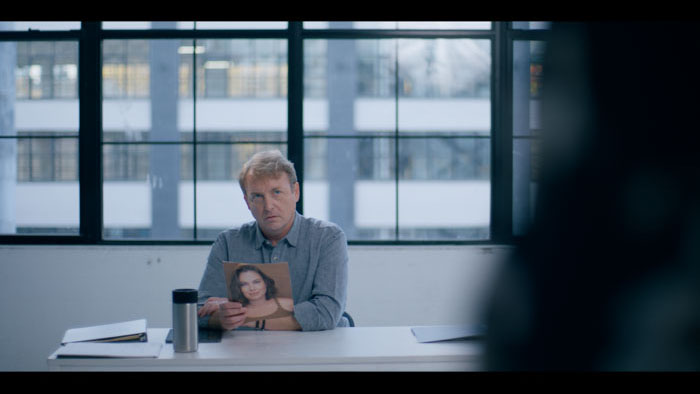 Andrew (AI Pagano) sits behind a table holding a headshot in The Last Act.