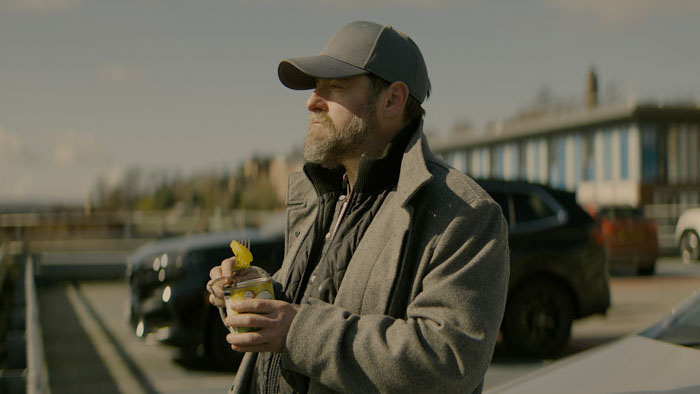 Jake (Andrew McGillan) eating canned pineapple in a parking area in A Maze in Truth.