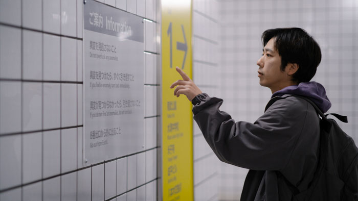 Kazunari Ninomiya as The Man points to the anomaly rules posted on the corridor wall in Exit 8.