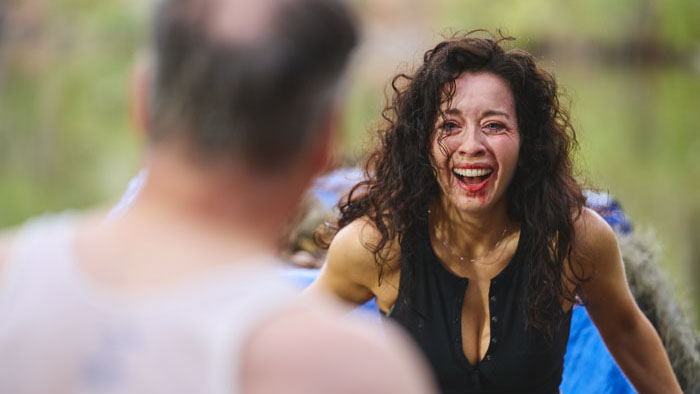 A woman with a bloodied face laughs intensely in a scene from G(L)ory Days.
