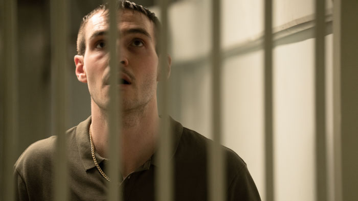 Barry McKenna (Éanna Hardwicke) stands behind bars looking upward in No Ordinary Heist. 