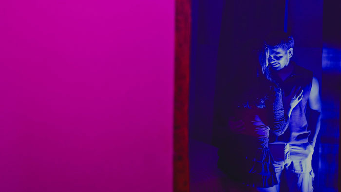 A couple stands together under neon lighting in Sin Salida.