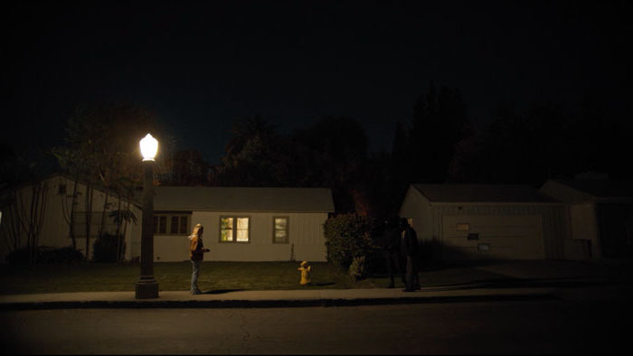 Rebecca (Nihan Gur) standing beneath a street lamp outside a suburban home at night in Steakout!