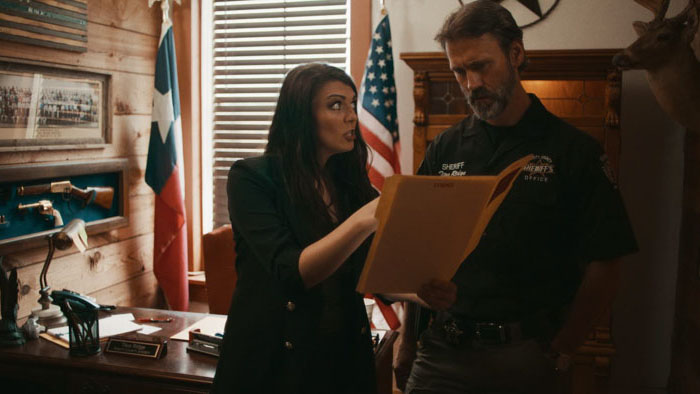 Mariella (Lizzie Camp) reviews a file with Sheriff Ridge (Terry Weaver) in The Beast of Trinity Texas.