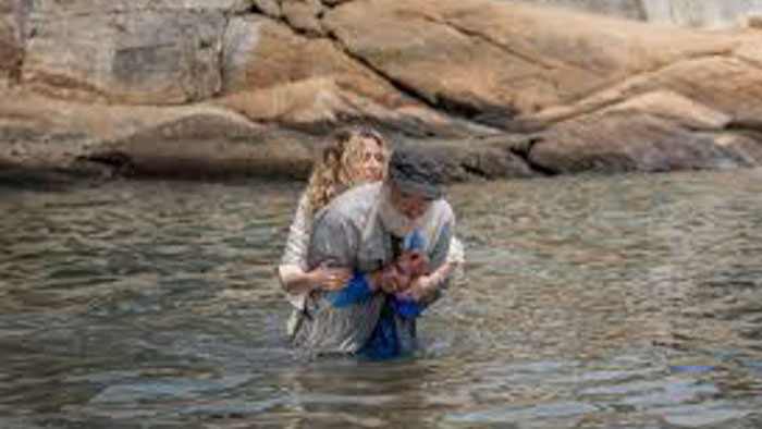 Two characters struggle in the water in a scene from Watching Mr. Pearson.
