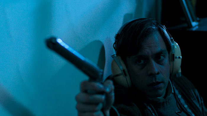 Chacal (Juan Cano) aims a gun while wearing headphones in A Yard of Jackals.