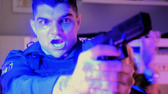 Officer Williams (Serge Usicov) aims his gun in a blue-lit scene from Not From Here.