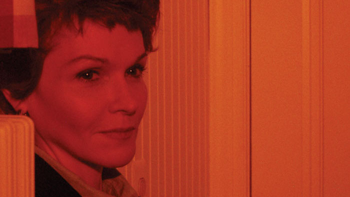 Deirdre Brennan as Rain, bathed in red light, peers from the shadows in the short film Rain.