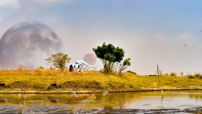 Adam and Bintu stand on an alien riverbank with a massive planet looming in the sky in The B.A.T.U. Project: Adam the First.