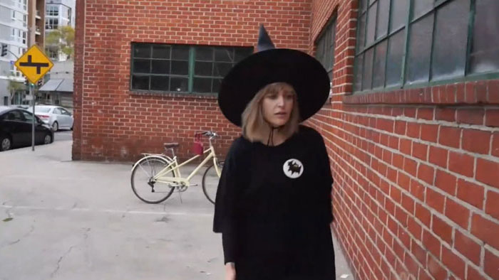 The Witch (Gina Romantini) walking beside a brick wall in The Latest Witch.