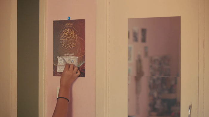 Eiman sits on a decorative rug surrounded by scattered family photographs in Villa 187.