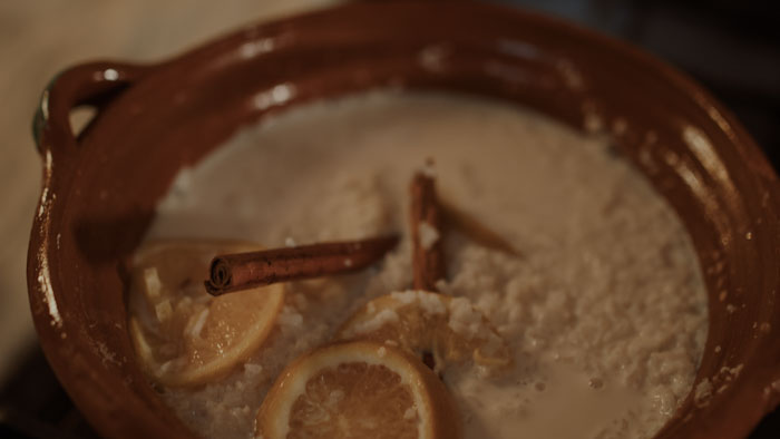 A clay pot of arroz con leche with cinnamon sticks and lemon slices in Where Roots Are Born.