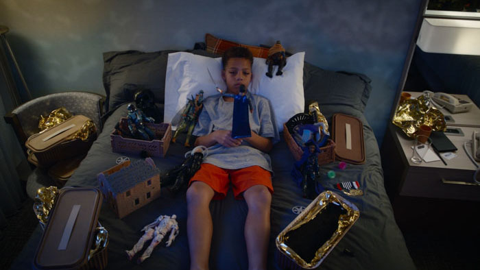 Milo (Austin Thomas) lies on a hotel bed surrounded by action figures and toys in Captain Milo.