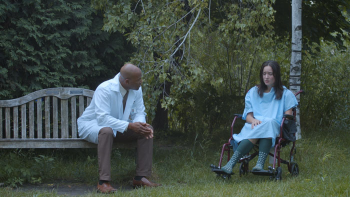 Jane (Amelia Barr) sits in a wheelchair as Dr. Smith (Jamel Anderson) speaks with her in a hospital garden in Jane's Not Here.