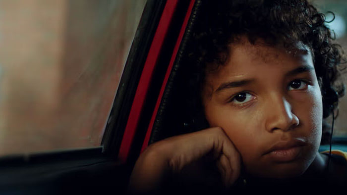 Hector (Emperor Kaioyus) rests his chin on his hand and stares out a car window in King of Games.
