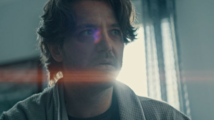 Cary (Michael Ursu) stares pensively toward a window with soft light and lens flare in Over Again.