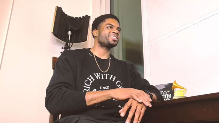 Omar Cook sits in a recording studio wearing a "Rich With God" sweatshirt in Royal: A Journey of Faith, Music, and Purpose.