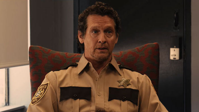 Sheriff Payton (Tom Reeping) sits in a chair in his uniform in a scene from Shrubs.