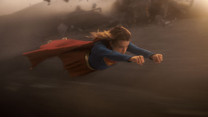 Kara Zor-El (Milly Alcock) flies through smoke and debris as Supergirl.
