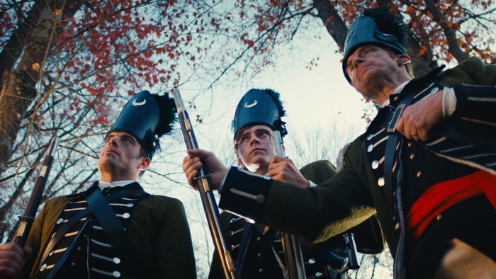 Three British Redcoat soldiers stand in formation holding muskets in the film 1780.