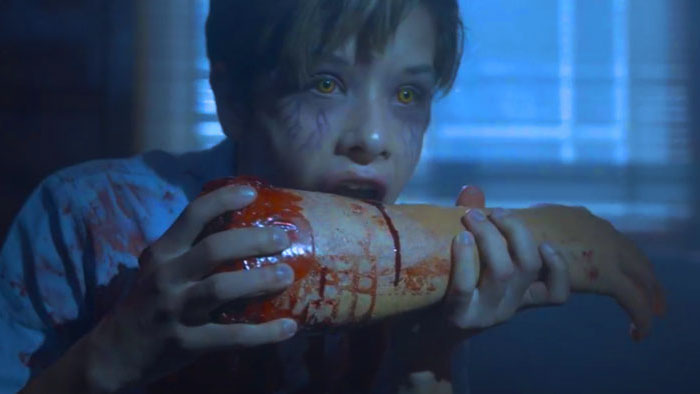 A young vampire with glowing eyes feeds on a bloody arm in Vampire Slayer.